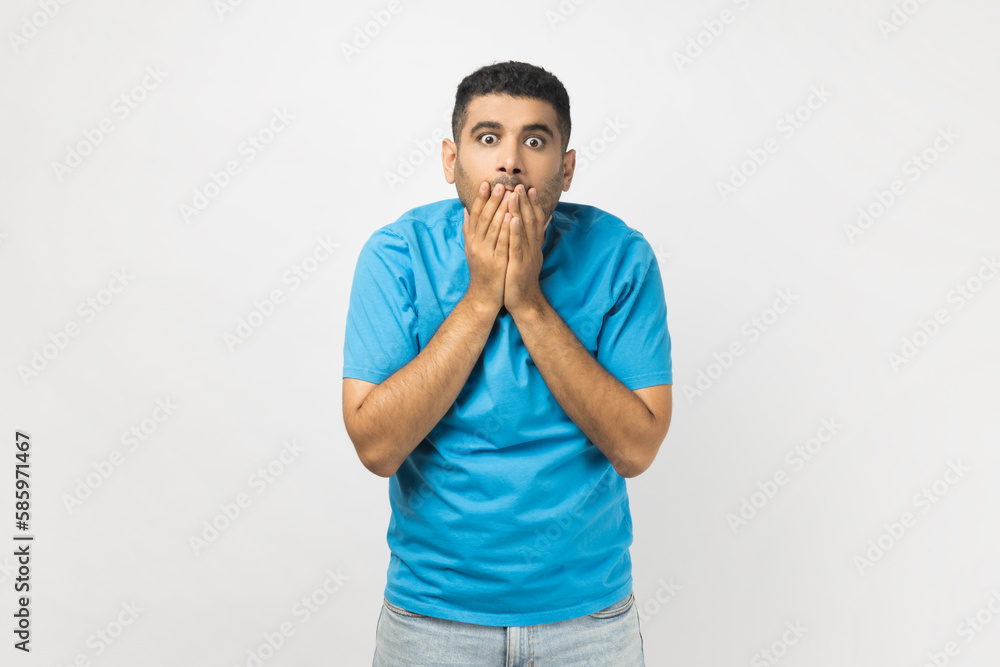 Astonished man looking at camera with big eyes, covering mouth with palms, sees something shocked. Astonished man looking at camera with big eyes, covering mouth with palms, sees something shocked.