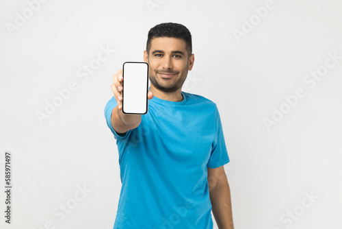 Cheerful satisfied man holding out smart phone with empty screen, copy space for advertisement.