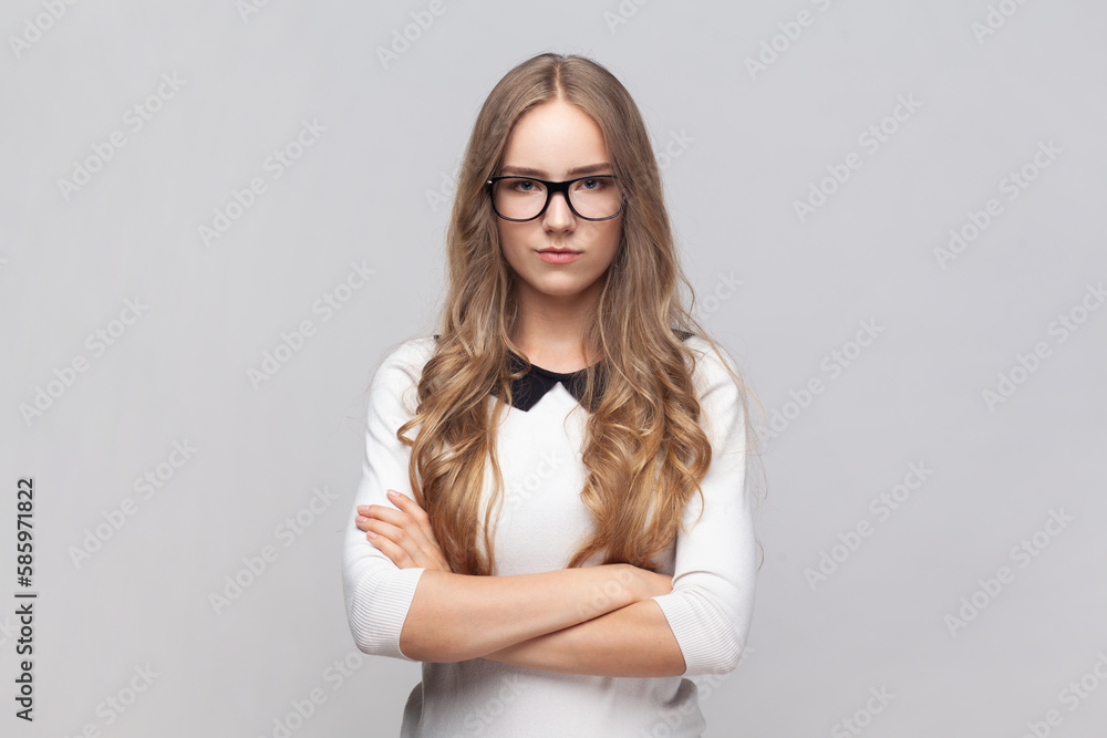 Serious strict woman in glasses standing looking at camera with bossy expression keeps hands crossed Serious strict woman in glasses standing looking at camera with bossy expression keeps hands crossed
