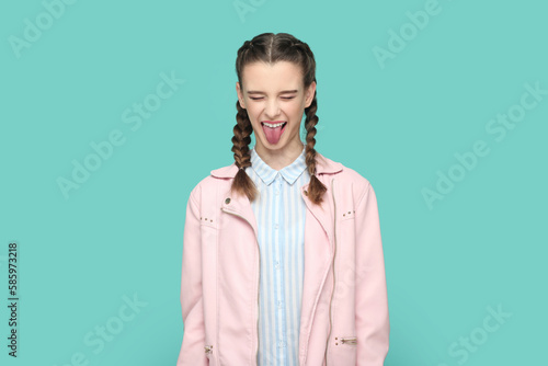 Funny childish teenager girl standing with closed eyes, sticking her tongue out, having fun.