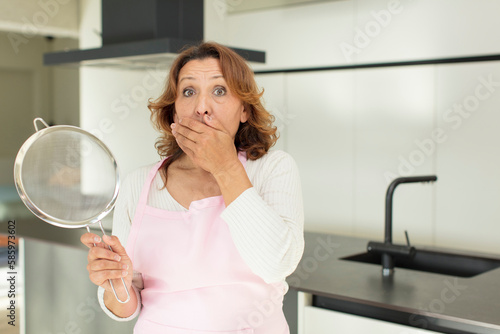 middle age pretty woman covering mouth with a hand and shocked or surprised expression. cooking at home concept