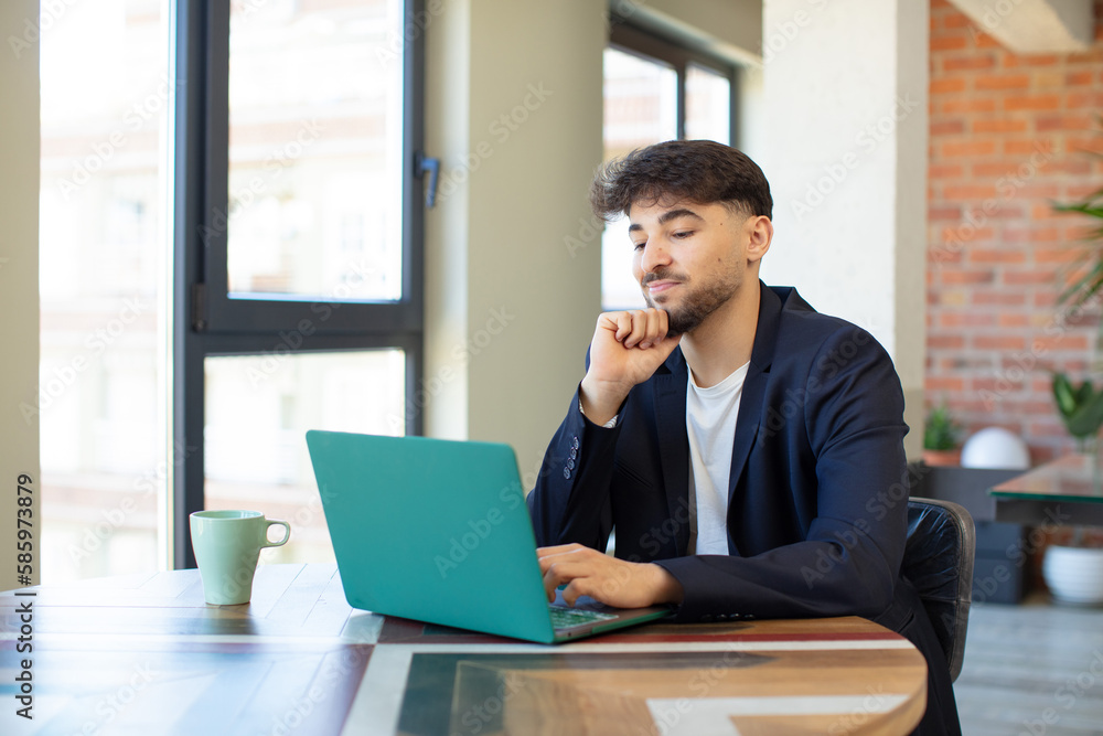 young handsome man smiling with a happy, confident expression with hand on chin. freelance concept with laptop young handsome man smiling with a happy, confident expression with hand on chin. freelance concept with laptop