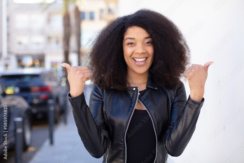 african american pretty woman smiling joyfully and looking happy, feeling carefree and positive with both thumbs up