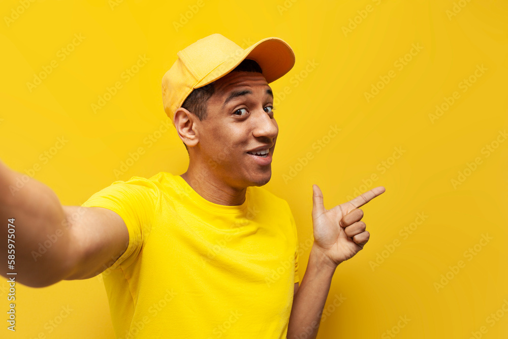 young african american delivery man in yellow uniform taking selfie and pointing at copy space young african american delivery man in yellow uniform taking selfie and pointing at copy space