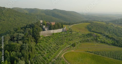 Aerial Panning Forward Shot Of Green Agricultural Field By Castello Di Brolio On Sunny Day - Tuscany, Italy photo