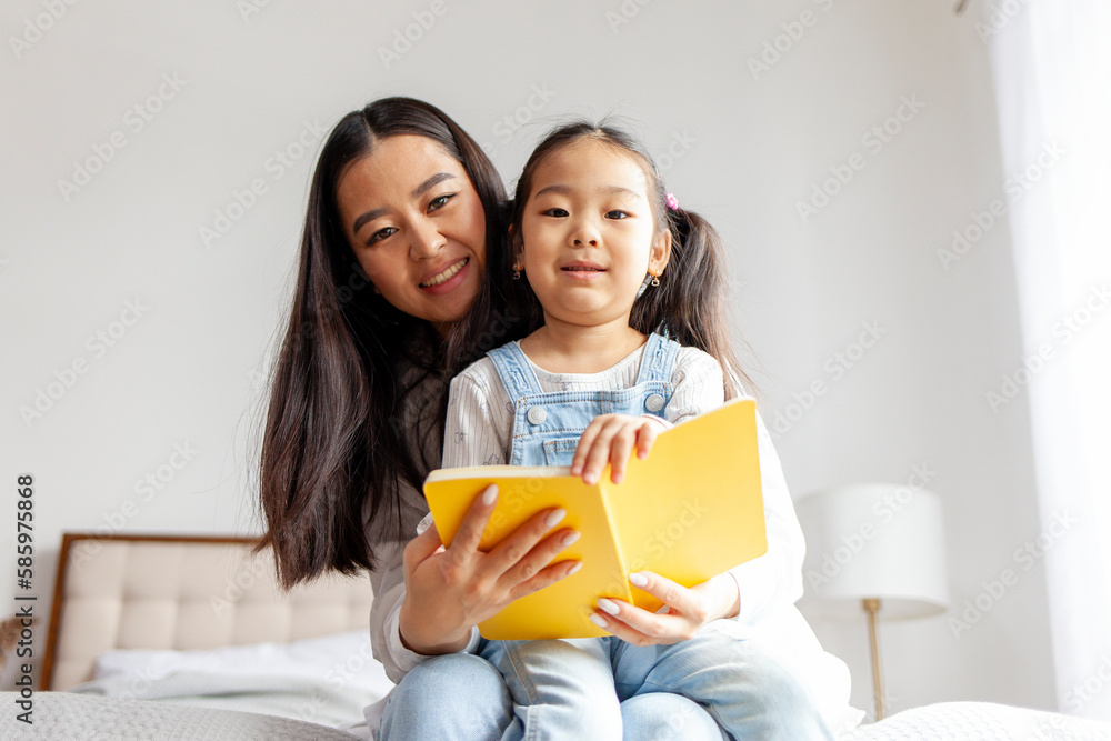 asian mother teaches daughter to read and write at home on bed, little korean girl writes in notebook with parent asian mother teaches daughter to read and write at home on bed, little korean girl writes in notebook with parent
