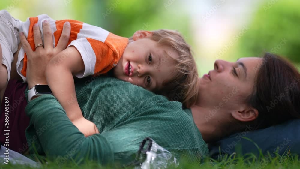 Mother lying on grass with child son outside at park during sunny beautiful day. Parent and kid bonding time outdoors. Parenting lifestyle happiness concept Mother lying on grass with child son outside at park during sunny beautiful day. Parent and kid bonding time outdoors. Parenting lifestyle happiness concept