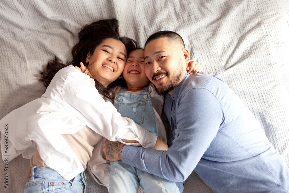 asian mom and dad hug little baby girl and lie on bed, happy korean family with daughter, concept of parental love asian mom and dad hug little baby girl and lie on bed, happy korean family with daughter, concept of parental love