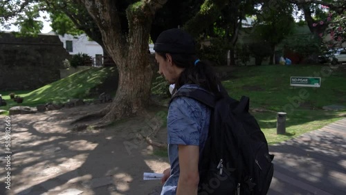 Follow shot of a young Latin man with a backpack as he walks through his college campus. Slow motion video. photo