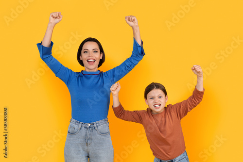 Excited Young Mother And Little Daughter Celebrating Success Over Yellow Studio Background