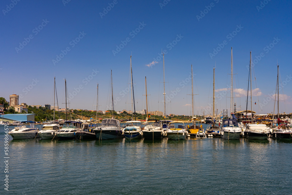 Small boats with motors and masts are docked next to the berth in the port.