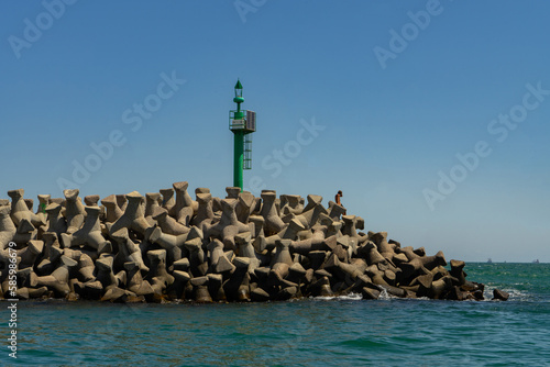 A green lighthouse at the end of the pier made of tetrapods or concrete blocks from the port of Tomis Constanta photo