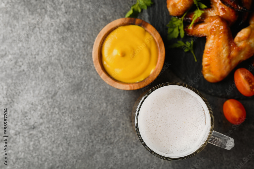 Mug with beer, delicious baked chicken wings and sauce on grey table, flat lay. Space for text Mug with beer, delicious baked chicken wings and sauce on grey table, flat lay. Space for text