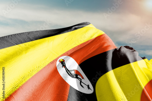 Uganda national flag cloth fabric waving on beautiful grey sky.