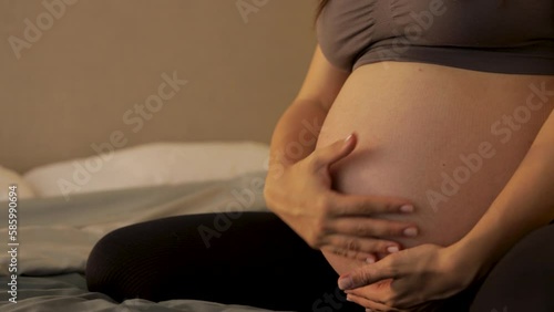 pregnant woman sitting on bed, stroking her stomach, close-up, blurred background