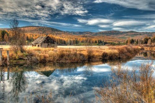 Beautiful nature scene with a lake surrounded by yellow hills with a small cabin under a blue sky