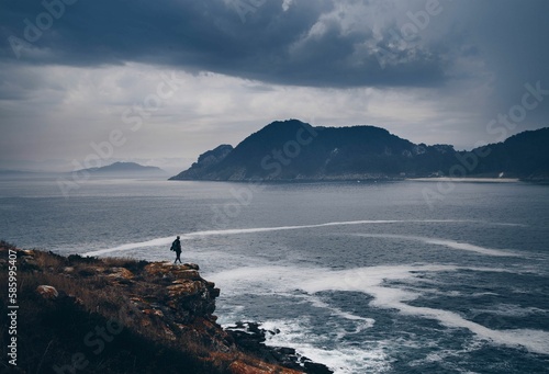 Seascape view with rocky cliffs, a man enjoying the view while standing on the beach