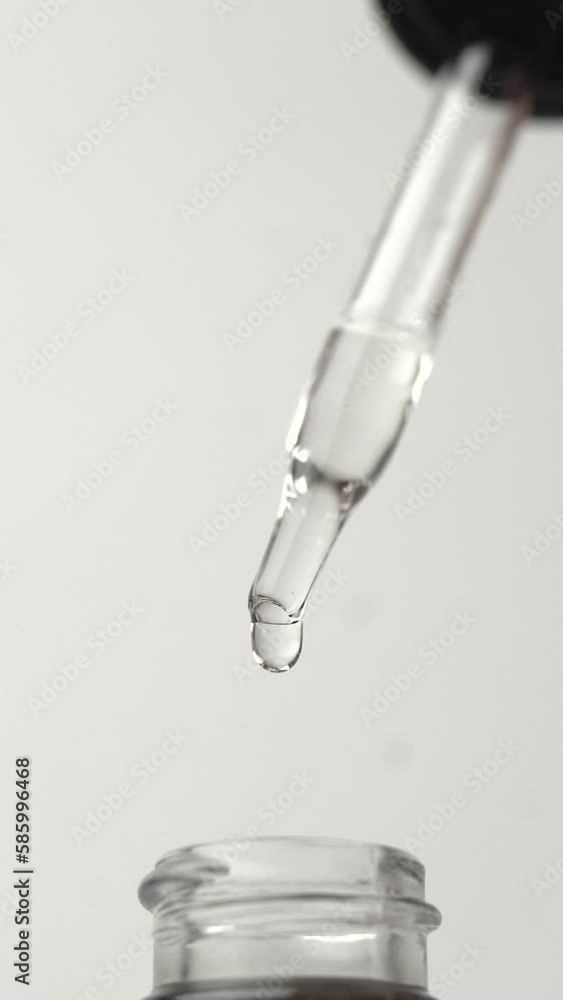Vertical shot of the oil drops falling from the pipette on the white background Vertical shot of the oil drops falling from the pipette on the white background