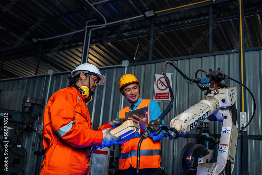 Engineer team service robot welding working in automation factory. People worker in safety suit work robotic arm software programming or replacing part in automated manufacturing industry technology Engineer team service robot welding working in automation factory. People worker in safety suit work robotic arm software programming or replacing part in automated manufacturing industry technology