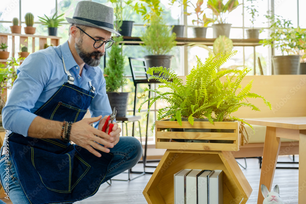 A senior man or grandfather with a mustache enjoys gardening for the tree at home after retirement