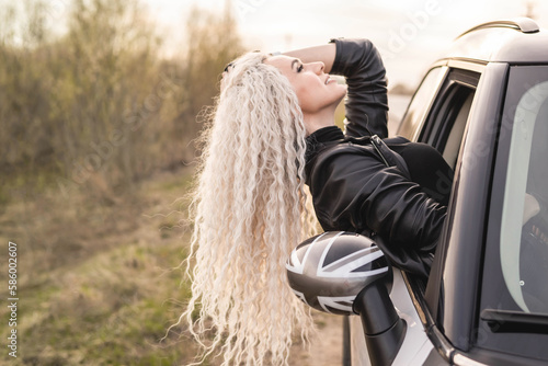 Happy curly fashion blonde woman sticking out from luxury car at countryside nature landscape
