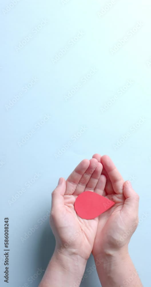 Vertical video of hands of caucasian man holding blood drop on blue background with copy space Vertical video of hands of caucasian man holding blood drop on blue background with copy space