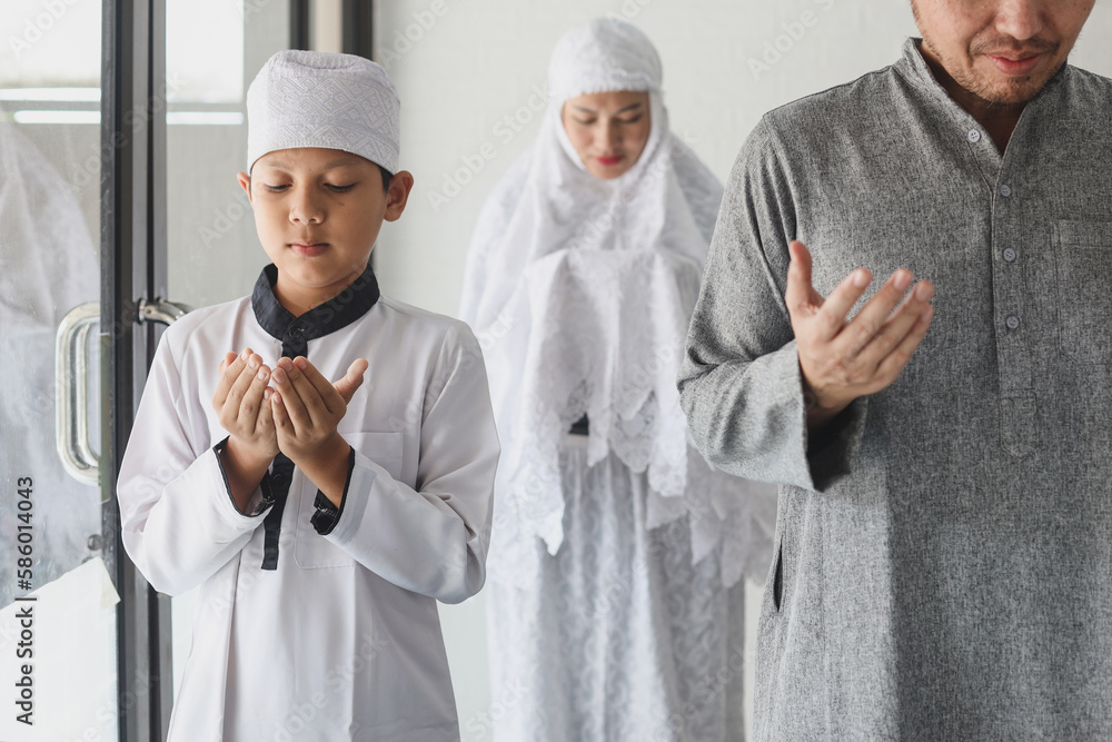 Asian muslim family praying dua together at mosque. Sholat or salah wearing white and hijab. Raising hands pray dua