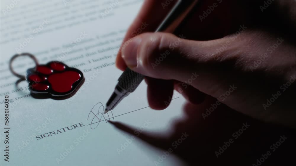 (Camera used: ARRI Alexa, shot in ARRIRAW, 50mm lens, 23.98 fps. Export: Rec.709, Apple Pro Res 422 HQ) Close up low angle shot of a female caucasian hand signing a document, with pet tag.