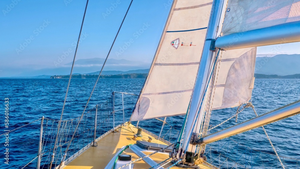 Obraz premium Coastal sailing, viewed from the foredeck of a sailboat with the jib and mainsail hoisted, on a beautiful sunny day. Puerto Galera, Philippines.