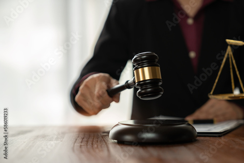 Female lawyer or legal advisor holding hammer on desk with contract documents and business agreement in law office justice concept