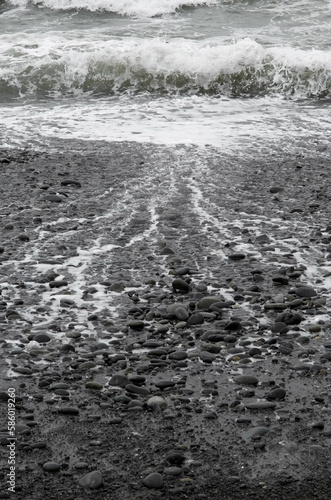 Sea foam ocean waves splashes and leaving traces on dark moody rocky beach