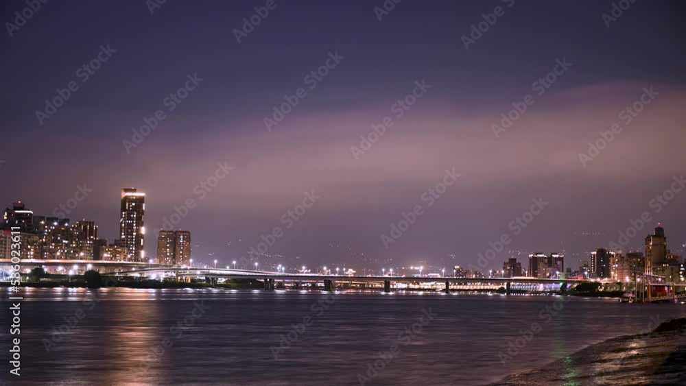 Clouds move in the night city. Colorful lights are reflected in the river water. Historic sights and trendy famous tourist attractions. Dadaocheng Wharf, Taipei, Taiwan Clouds move in the night city. Colorful lights are reflected in the river water. Historic sights and trendy famous tourist attractions. Dadaocheng Wharf, Taipei, Taiwan
