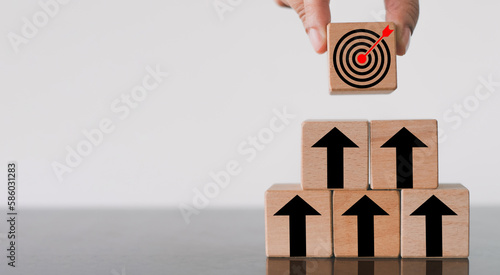 Goal Achievement and Purposefulness,challenge in busiess concept.,Hand  arranges a wooden block with dartboard icon stack in pyramid shape over white background with copyspace. photo