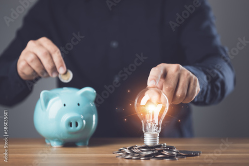 Business, Financial and money planning, Clever thinking about money saving for future and retirement, Man holding light bulb with coin pile and adding coin to piggy bank on the table.