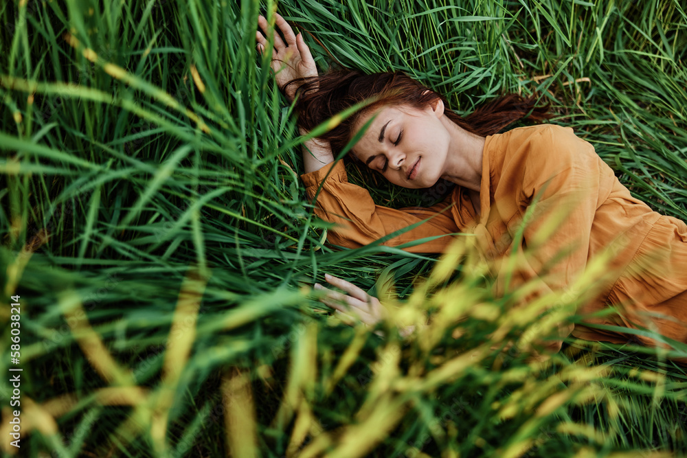 a pleasant woman in a long orange dress resting lying in the tall grass with her eyes closed in sunny weather at sunset with her arms outstretched. Street photography, the theme of privacy with nature a pleasant woman in a long orange dress resting lying in the tall grass with her eyes closed in sunny weather at sunset with her arms outstretched. Street photography, the theme of privacy with nature