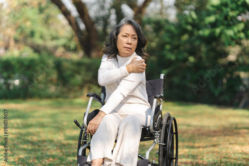 Asian old woman sitting on a wheelchair outdoors in the park have shoulder pain