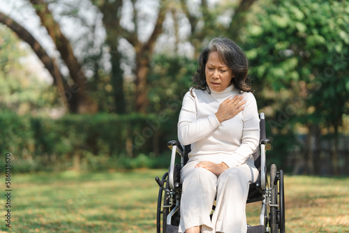 Asian old woman sitting on a wheelchair outdoors in the park There is pain in the heart and myocardium.