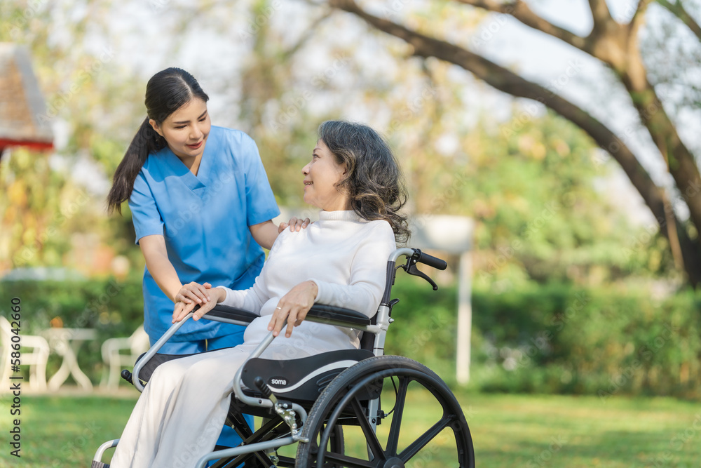 Young asian care helper with asia elderly woman on wheelchair relax together park outdoors to help and encourage and rest your mind with green nature. Young asian care helper with asia elderly woman on wheelchair relax together park outdoors to help and encourage and rest your mind with green nature.