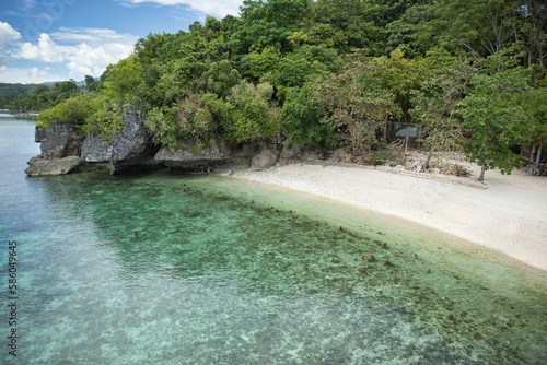 Idyllic, secluded beach of Siquijor in the Philippines with white sand and crystal clear water in a small bay with trees and cliffs.
