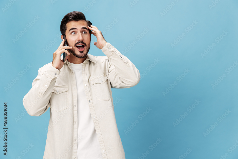 Portrait of a brunette man talking on the phone close-up mobile and internet online, animation open mouth, on a blue background in a white T-shirt, copy space Portrait of a brunette man talking on the phone close-up mobile and internet online, animation open mouth, on a blue background in a white T-shirt, copy space