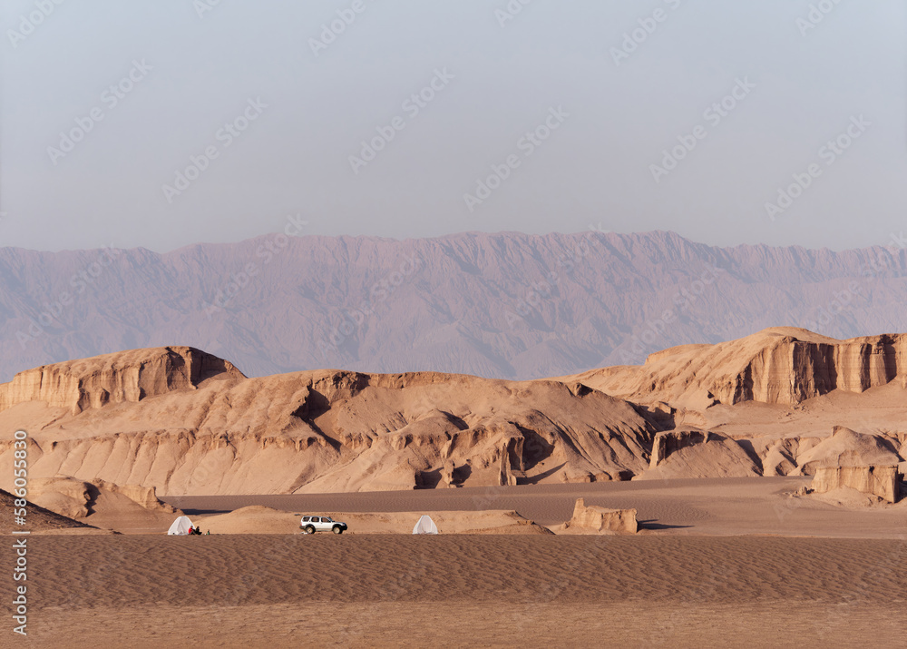 Peaceful view of the beautiful Dasht-e Lut Desert and its rock formations (Kaluts) and tent and jeep in the distance, Kerman Province, Iran