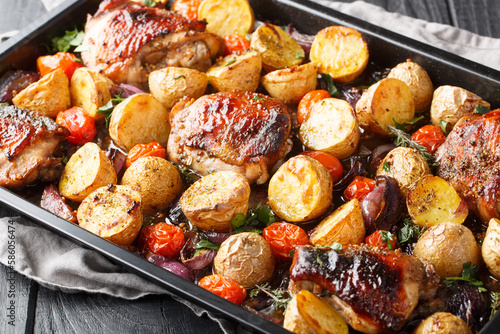 Obraz na płótnie Italian barbecue balsamic chicken with potatoes, red onion and tomatoes close-up on a baking sheet on a wooden table
