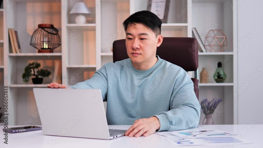 Cheerful focused businessman, office worker opening laptop to begin working. Asian male looks into camera and smiles. Positive side of working in office, importance of being focused and motivated. Cheerful focused businessman, office worker opening laptop to begin working. Asian male looks into camera and smiles. Positive side of working in office, importance of being focused and motivated.