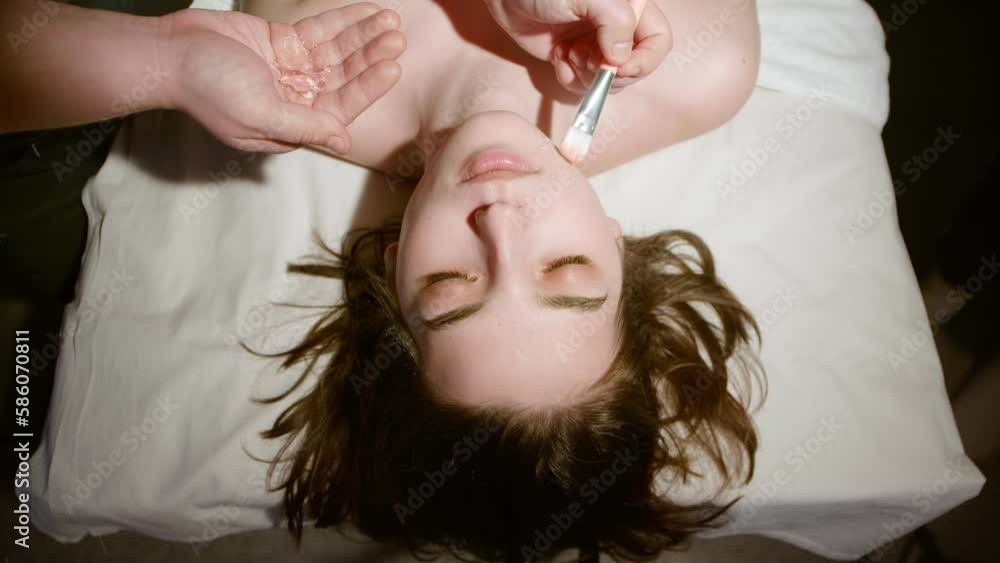 The cosmetologist applies a moisturizing mask to a woman's face. The cosmetologist applies a moisturizing mask to a woman's face.