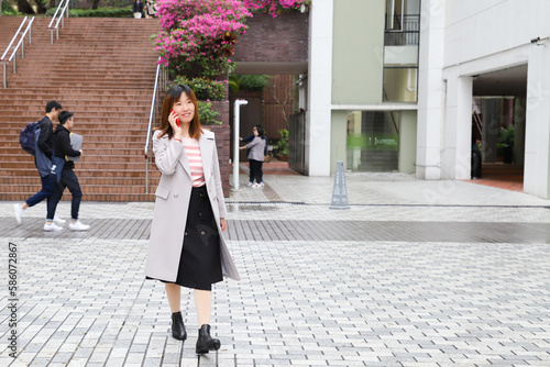 Photography female Chinese student wearing stylish grey overcoat chatting over phone in univ
