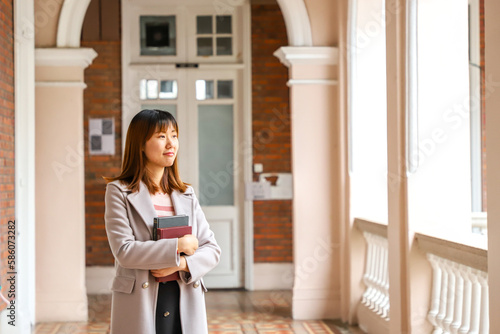 Фотография female Asian student wearing stylish grey overcoat with books in university camp