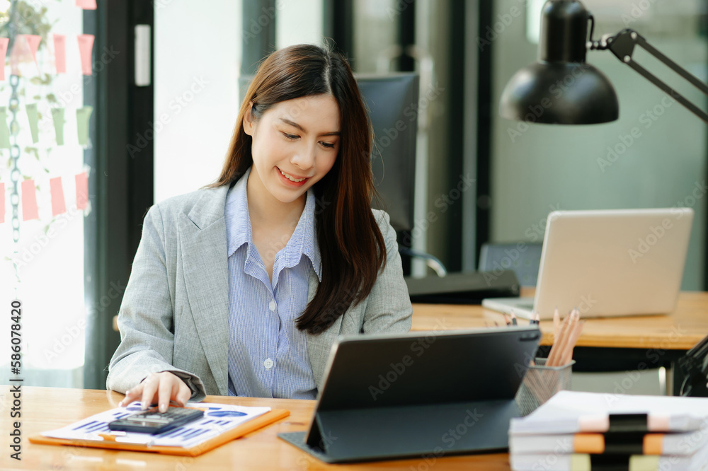 Asian woman with a smile standing holding notepad and tablet at the modern office.. Asian woman with a smile standing holding notepad and tablet at the modern office..