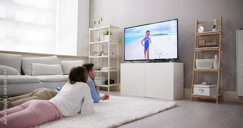 Young Couple Watching TV While Sitting On Sofa In Living Room Young Couple Watching TV While Sitting On Sofa In Living Room