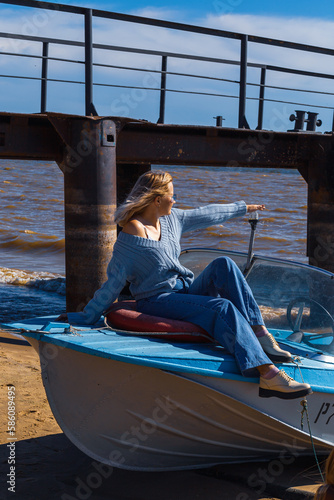 Portrait of a young beautiful girl in a blue sweater and jeans is on a boat near the river pier

