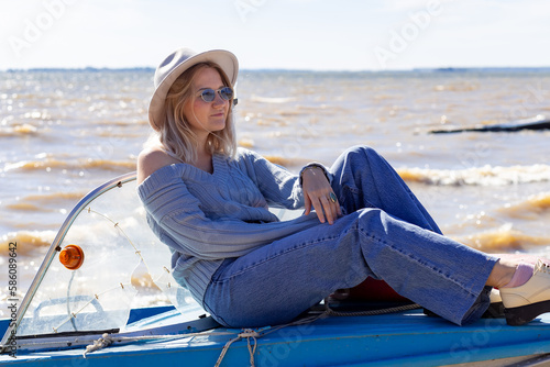 Portrait of a young beautiful girl in a blue sweater and jeans is on a boat near the river pier

